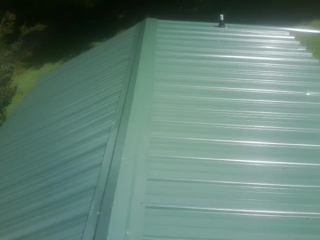 New green metal panels meeting at the ridge of a roof — Flat Roof Repair work by our crew in Hazlehurst